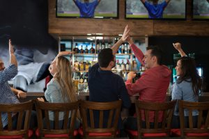 Happy group of friends watching sports at the bar and drinking beer